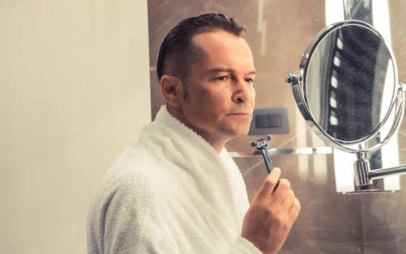 Man thinking while holding a razor, considering head shaving FAQs.